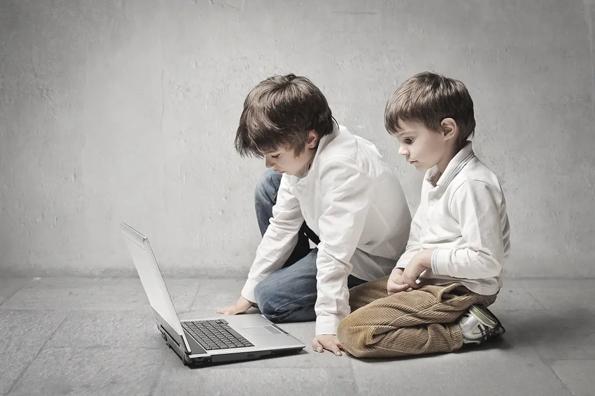 Two little boys sitting with a laptop in a grey room