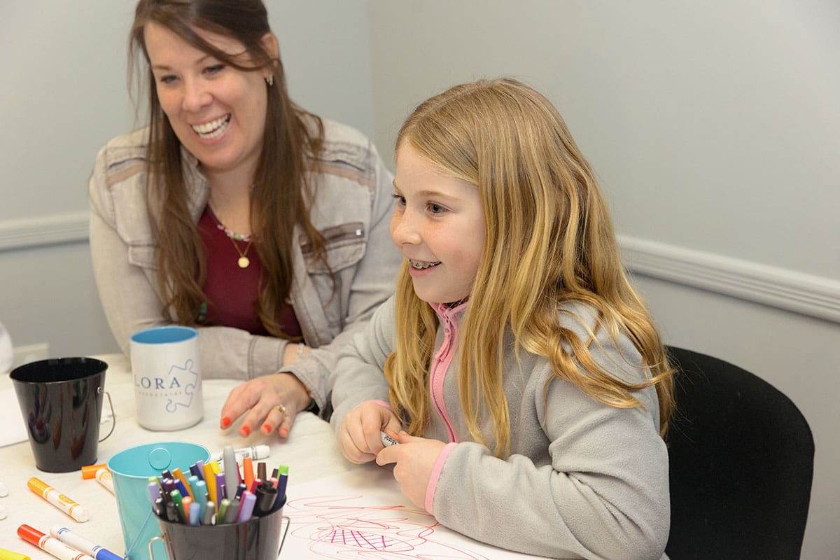 A child and a therapist sitting and drawing and smiling and laughing together during art therapy at Flora and Assosiates