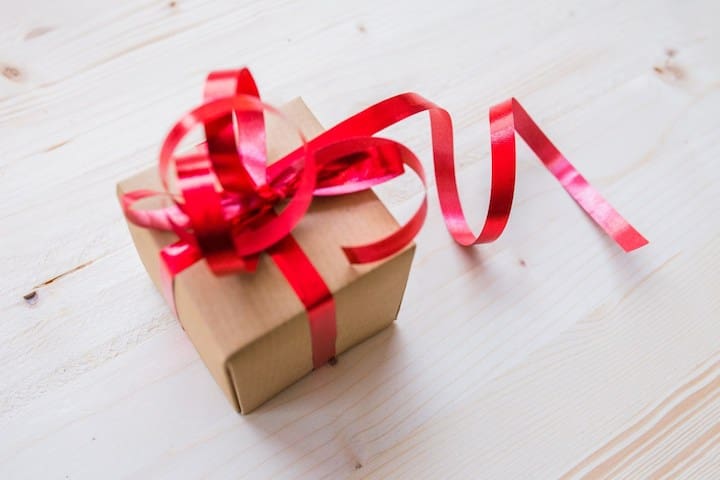 A gift box being wrapped with ribbon.