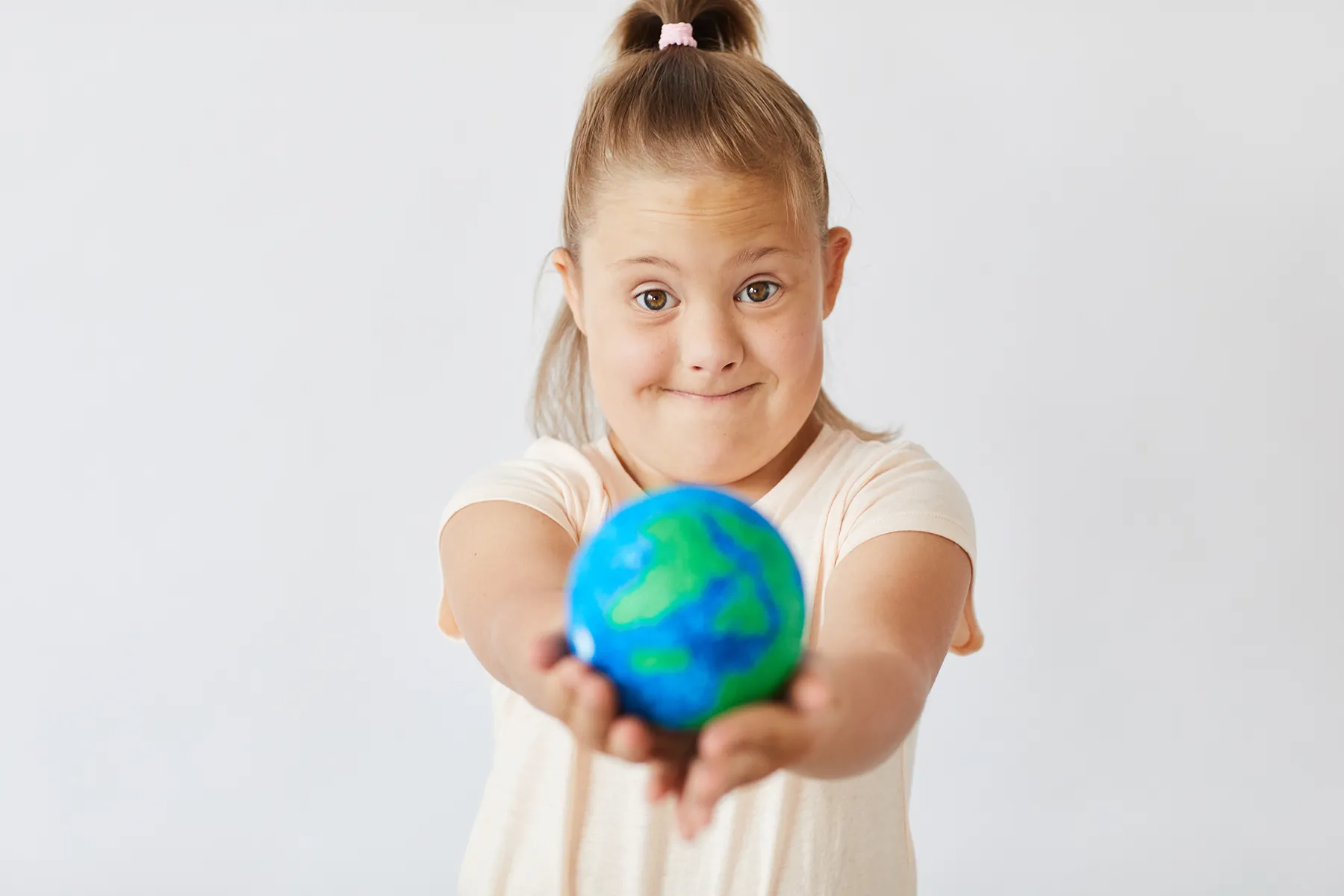 down-syndrome-girl-2025-02-11-15-42-06-utc Young girl with Down syndrome smiling and holding a small globe forward, symbolizing inclusion, global awareness, and World Down Syndrome Day.