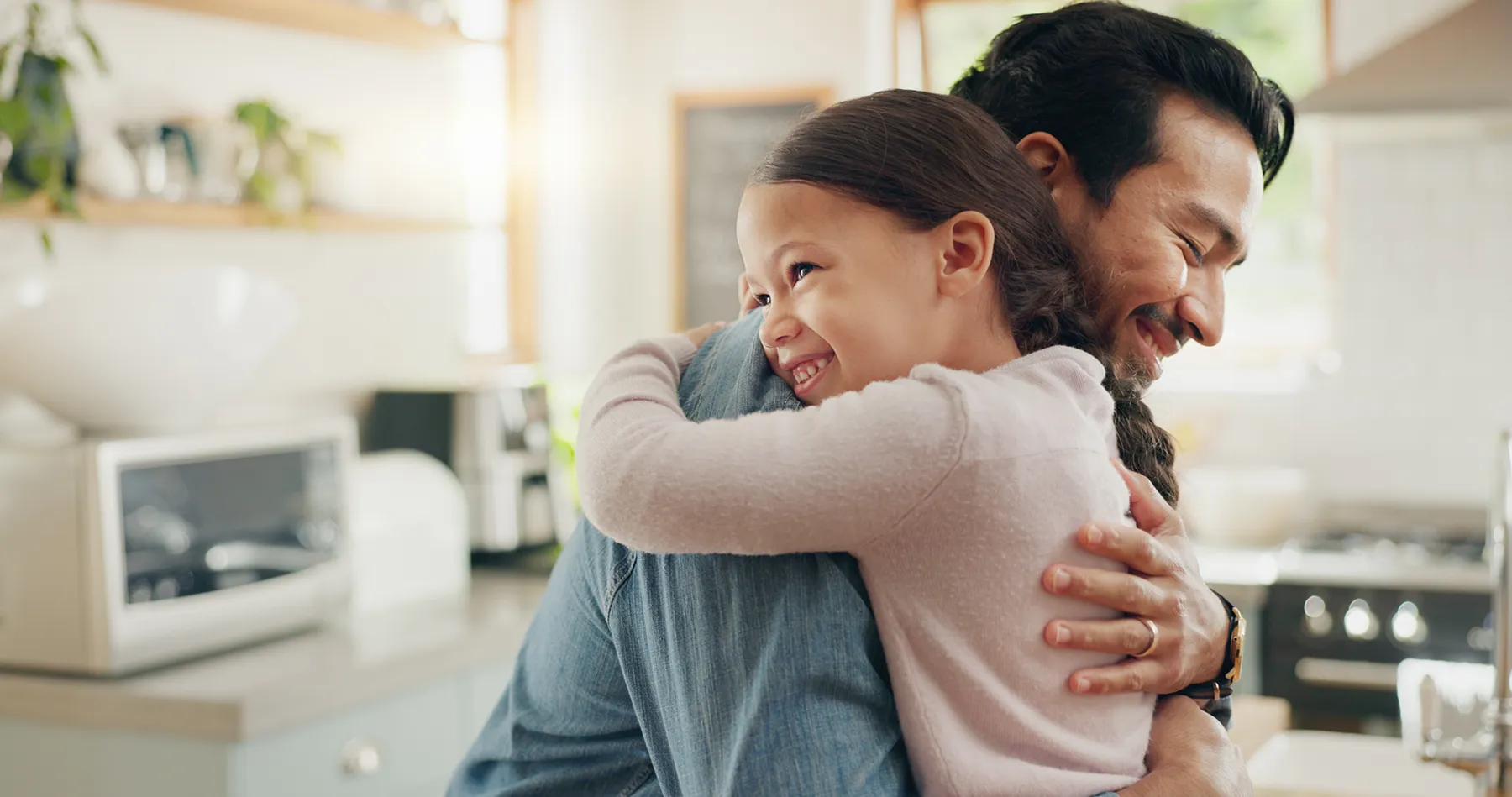 family-father-and-daughter-hug-in-the-kitchen-for-2025-04-06-07-40-57-utc Father and daughter share a warm hug in a bright kitchen, reflecting emotional health, stress relief, and the fulfillment of a child’s emotional need for connection.