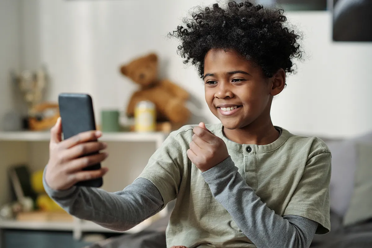 Happy schoolboy holding smartphone in front of himself and taking selfie, (social media boundaries)