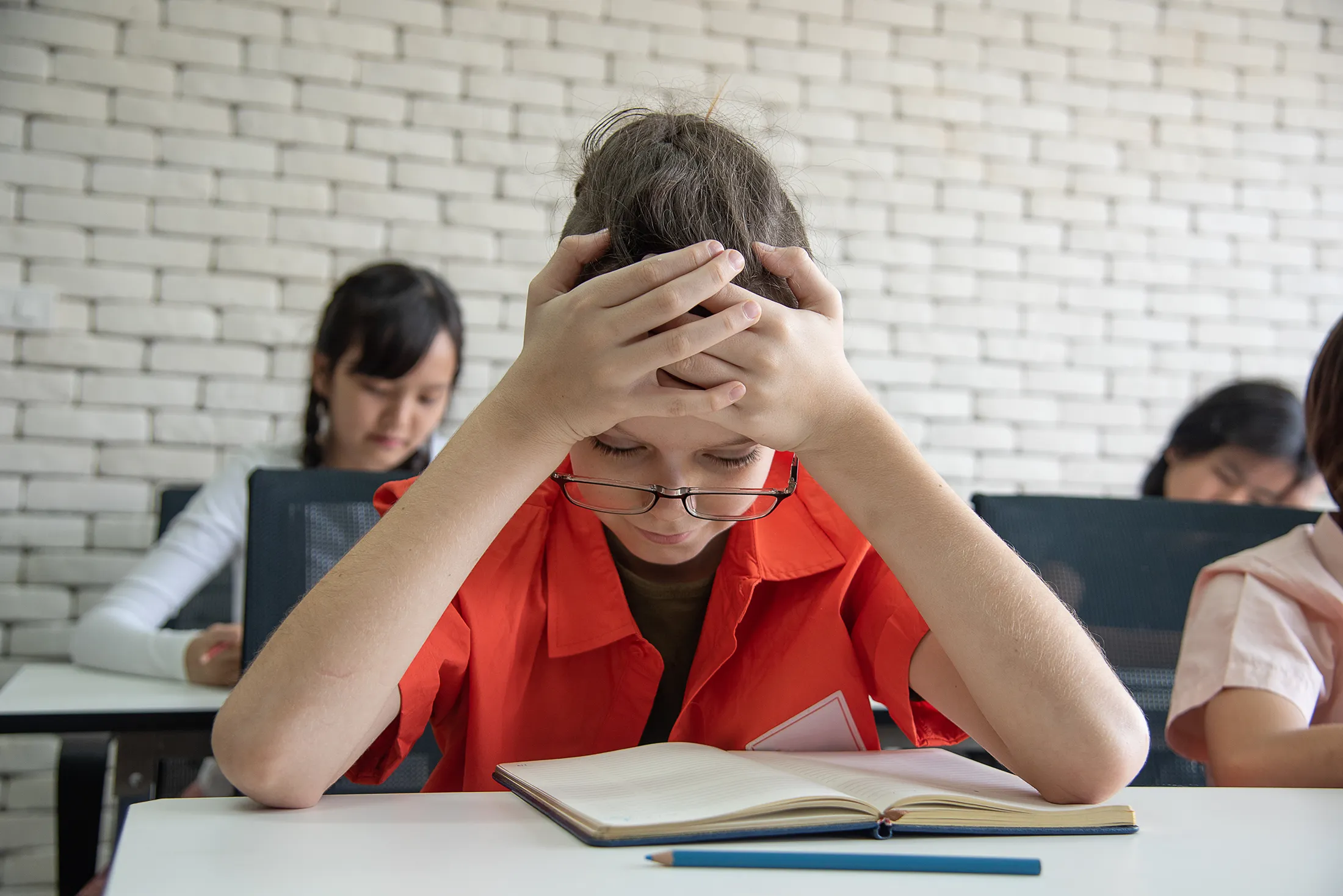 Stressed student holding their head while trying to read a book in a classroom.